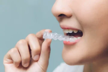A close-up of a person holding a clear dental aligner near their mouth, preparing to fit it over their teeth.